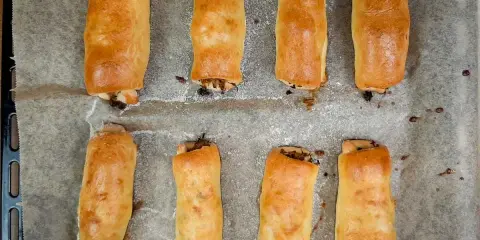 Osiem złotych pasztecików z ciasta drożdżowego, idealne ciasto na paszteciki, ułożonych na papierze do pieczenia.