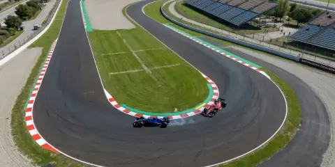 Dos coches de F1 compiten en una curva cerrada de los circuitos F1, uno azul derrapa y el otro rojo acelera.