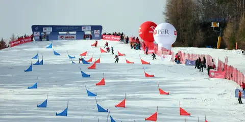 Zawodnicy snowboardu pokonują trasę z czerwonymi i niebieskimi tyczkami na stoku Jaworzyny Krynickiej.