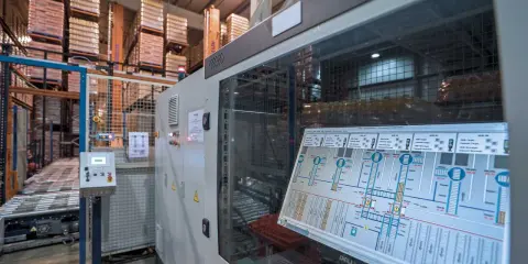 Schermata di un sistema di controllo plc in un magazzino automatizzato, con scaffali carichi di merce sullo sfondo.