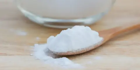 Łyżka z białym proszkiem, który może pomóc na zgagę. W tle szklane naczynie z tym samym produktem.