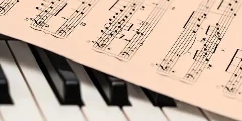 Partytura muzyczna na klawiaturze pianina. Widoczne nuty i klucze, które oddają bogate **cechy muzyki barokowej**.