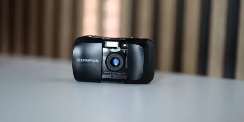 Czarny aparat Olympus mju:-1 z obiektywem 35mm 1:3,5 na jasnym blacie.