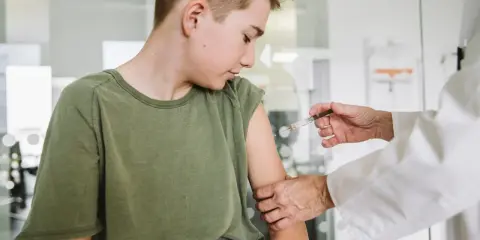 Chłopiec w zielonej koszulce otrzymuje zastrzyk od lekarza w białym fartuchu.