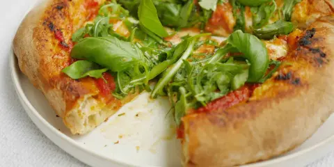 En närbild av en pizza med ruccola och basilika. Perfekt för ett enkelt pizzasås recept.