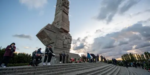 Uroczystość przy Pomniku Obrońców Wybrzeża na Westerplatte w Gdańsku. Warty honorowe, wieńce i zgromadzeni ludzie.