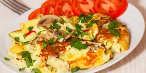 Pyszny omlet jajeczny z pieczarkami i natką pietruszki, podany z plastrami pomidora. Idealny na śniadanie.