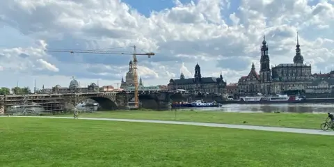 Grüne Wiese mit Blick auf die Elbe, die Brücke und die Frauenkirche. Ein Radfahrer genießt die Aussicht, um Dresden zu erleben.