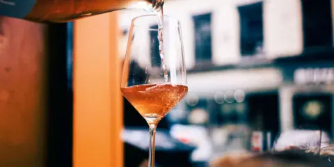 En flaska häller upp ett bubbligt, roséfärgat pet nat i ett elegant glas. En härlig kväll väntar.