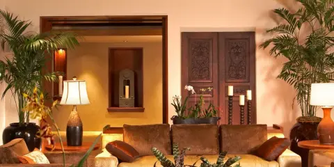 Salotto accogliente con divani in velluto, piante tropicali e porte intagliate in legno scuro, che evocano un caldo **stile coloniale**.