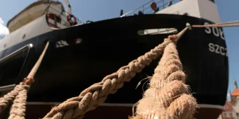 Gros cordage tressé, essentiel au point d'amarrage d'un navire noir et blanc sous un ciel bleu.