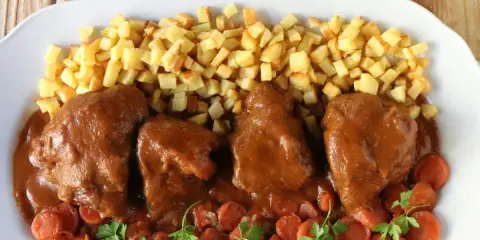 Delicioso jarrete de ternera estofado en salsa, acompañado de patatas fritas y zanahorias.