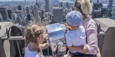 Familia disfrutando de las vistas de Nueva York con niños, explorando la ciudad a través de un telescopio.