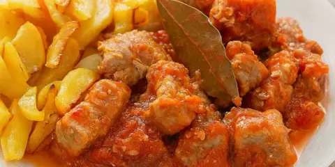 Sabroso magro con tomate, trozos de carne tierna en salsa de tomate, acompañados de patatas fritas doradas.
