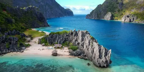 A secluded beach in the Philippines, with turquoise waters, limestone cliffs, and small huts. A perfect gay getaway in paradise.