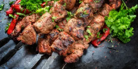 Soczyste kawałki mięsa na szpadach, przypominające kofta kebab, podane z pieczoną papryką i świeżą natką pietruszki.