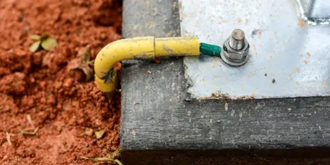 Connexion de la prise de terre maison à une structure métallique, assurant la sécurité électrique. Le câble jaune est relié à une cosse verte, fixée par un boulon.