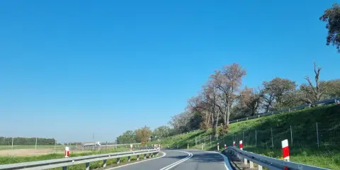 Słupki na autostradzie wyznaczają zakręt drogi. Jasne niebo i zielone pobocze tworzą malowniczy krajobraz.