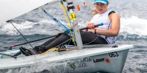 Jeune femme concentrée naviguant en deriveur solo, le bateau #063 fend les vagues.