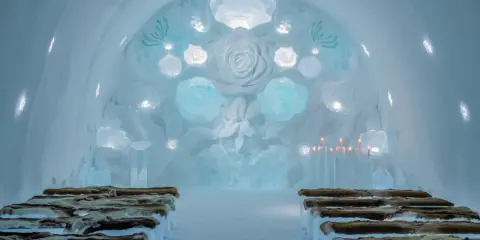 Vacker iskyrka i ett igloo hotell Sverige. Bänkar av is med renskinn, isrosor och levande ljus skapar en magisk atmosfär.