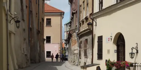 Wąska, brukowana uliczka w Lublinie z kamienicami i kilkoma spacerującymi osobami.