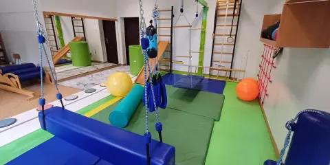 Sala terapeutyczna z huśtawkami, materacami i sprzętem do ćwiczeń, wspierająca rozwój dzieci z zaburzeniem integracji sensorycznej.