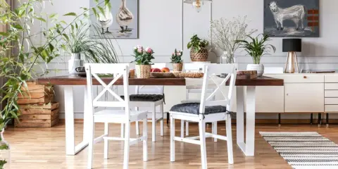 Comedor con mesa de madera oscura y sillas blancas, un ejemplo perfecto de cómo combinar muebles blancos y madera oscura. Plantas y cuadros decoran el espacio.