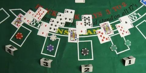 Stół do gry w blackjacka, karty i żetony. Widać karty z numerami i figurami, a także napisy "BLACKJACKS 3 TO 2" i "stand on all 17's".