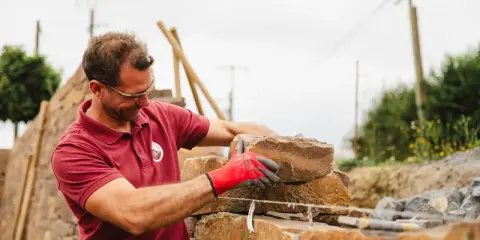 Un maçon, ganté de rouge, pose une pierre pour construire un mur en Corse.