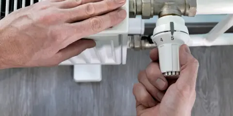 Mano ajusta el termostato de un radiador. El radiador solo calienta la mitad derecha, indicando un posible problema.