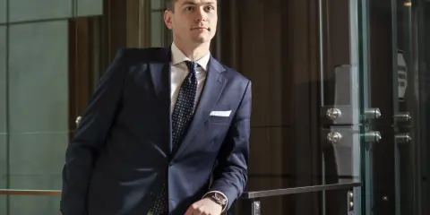 Mężczyzna w granatowym garniturze i krawacie opiera się o poręcz.