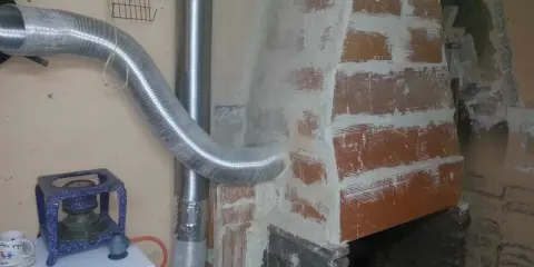 Instalación de tubo flexible para aprovechar calor de chimenea. Se ve una estufa azul y una chimenea de ladrillo.