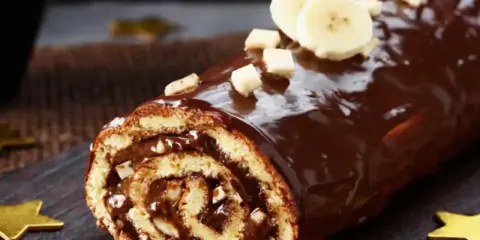 Bûche roulée au chocolat, garnie de crème et recouverte d'un glaçage chocolat beurre brillant, décorée de rondelles de banane et de noisettes concassées.