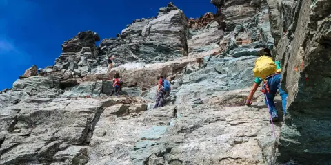 Alpinisti scalano la roccia sul Monviso, seguendo la via normale. Un'avventura sotto il cielo azzurro.