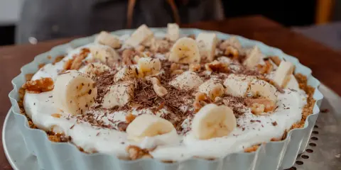 Tarte banane caramel onctueuse, garnie de rondelles de banane, noix et copeaux de chocolat. Un délice gourmand.