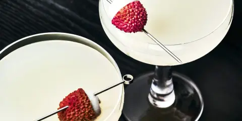 Dwa eleganckie drinki z liczi, ozdobione owocami na patyczkach, kuszą swoim orzeźwiającym wyglądem.
