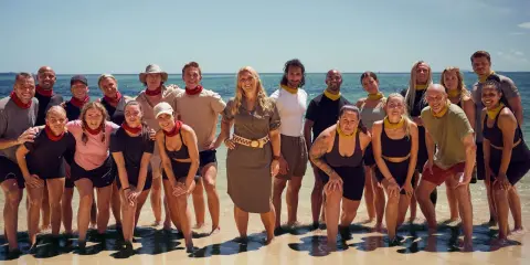En grupp glada robinson deltagare poserar på en strand med havet i bakgrunden.