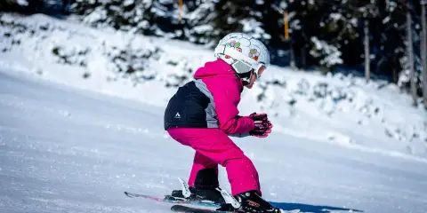 Dziecko w różowym kombinezonie i kasku zjeżdża na nartach. Idealne narty dla dziecka 130 cm to te, które zapewnią mu stabilność i radość z jazdy.
