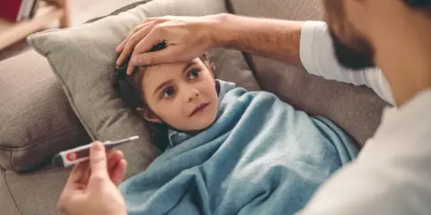 Ojciec sprawdza temperaturę chorej córki. Opieka na dziecko do ilu lat? Zawsze, gdy jest chore i potrzebuje troski.