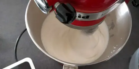 Un robot pâtissier rouge mélange une crème onctueuse, étape clé pour réussir une pâte à bombe aérienne.