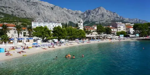 Słoneczna plaża w Baška Voda, z turkusową wodą i górami w tle. To idealne miejsce na relaks i odkrywanie atrakcji.