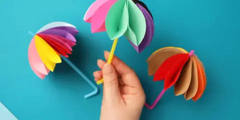 Bunte Papier-Regenschirme, tolle bastelideen einfach und schnell für Kinder. Ein gelber Schirm wird von einer Hand gehalten.