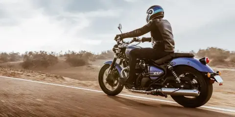 Motocyklista w skórzanej kurtce pędzi na niebieskim **super meteor 650** przez pustynny krajobraz.
