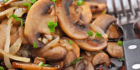 Jak usmażyć pieczarki? Na talerzu aromatyczne, podsmażone pieczarki z cebulką i szczypiorkiem, gotowe do jedzenia.