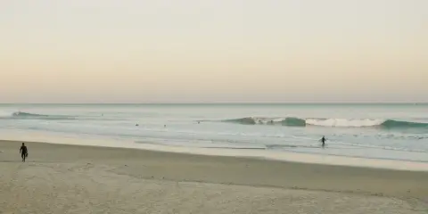 Ein Surfer geht ins Meer, um Cornwall zu surfen. Sanfte Wellen brechen am Strand.