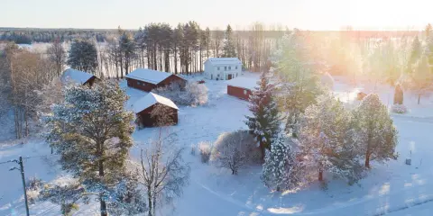 Snötäckt gård med vita och röda byggnader. Solen lyser på ett nybyggt hus, en idyllisk vy som ger tankar om framtida fastighetsavgift.