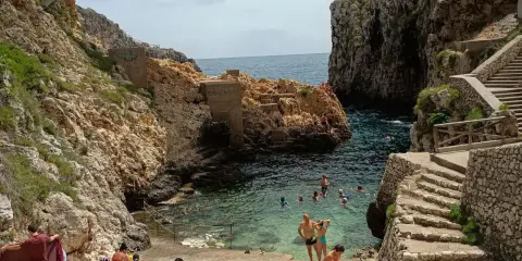 Santa Maria di Leuca: cosa vedere? Una caletta rocciosa con gente che nuota e si rilassa, con scalinate di pietra che scendono verso il mare cristallino.