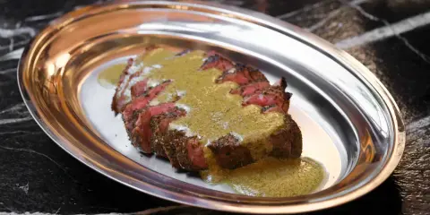 Tranché de bœuf, nappé d'une sauce verte, une spécialité parisienne servie sur un plateau métallique.