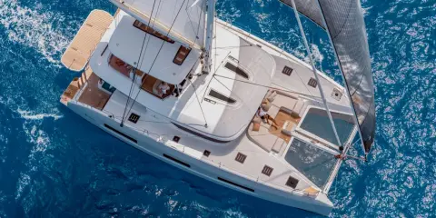 Un catamaran sans voile glisse sur l'eau bleue. Une personne se repose sur le pont, profitant du soleil.