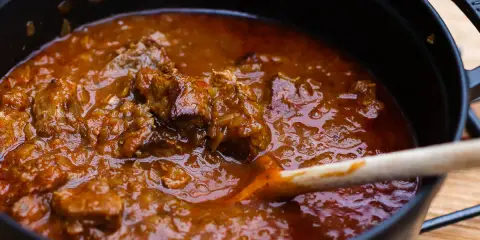 Ein dampfender Topf mit zartem Wiener Saftgulasch, das mit einer Holzschaufel umgerührt wird.